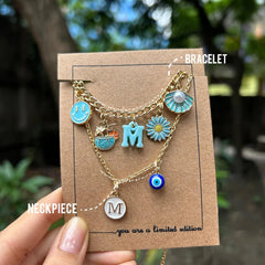 Oceanic Charm Stack: Blue bracelet and necklace with personalized initial, smiley charm, coconut water, flower, shell, and evil eye
